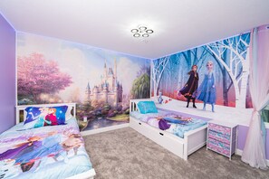 Ein Schlafzimmer mit Wandgemälde von Burg und Figuren, einem Bett mit Disney-Betttuch und einem Schreibtisch mit Schubladen.