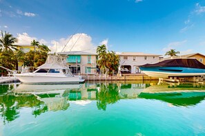 Boats docked at a tranquil marina surrounded by tropical-style buildings with flat roofs and large windows.
