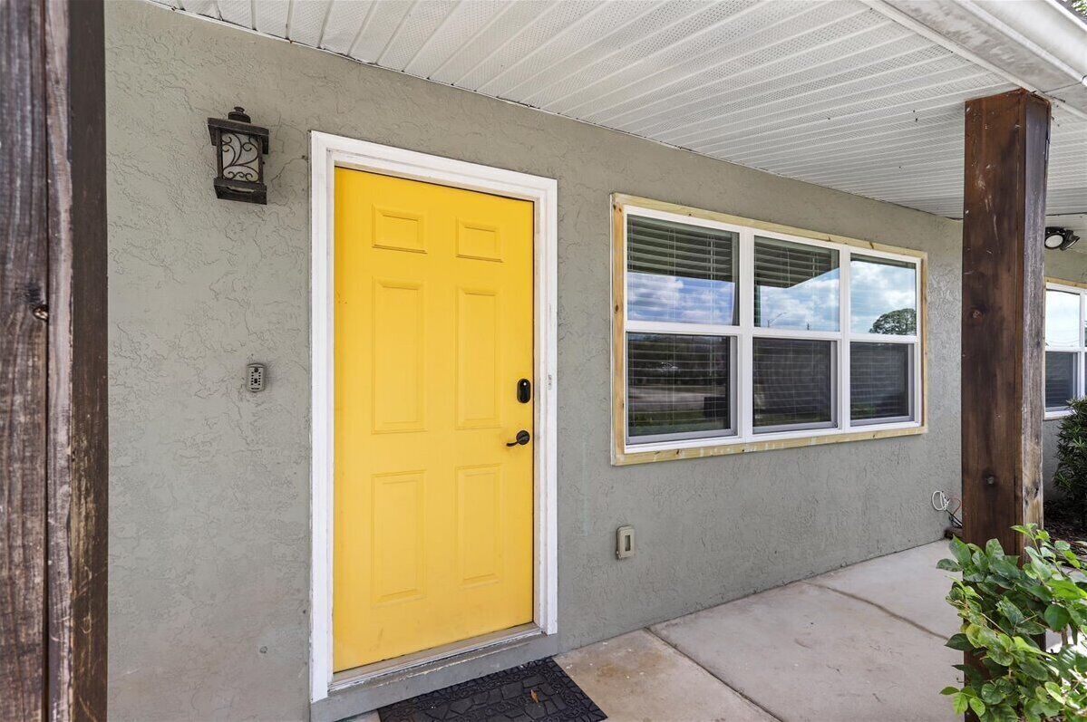 A house with a yellow front door, a window with blinds, and a porch with a wooden post.