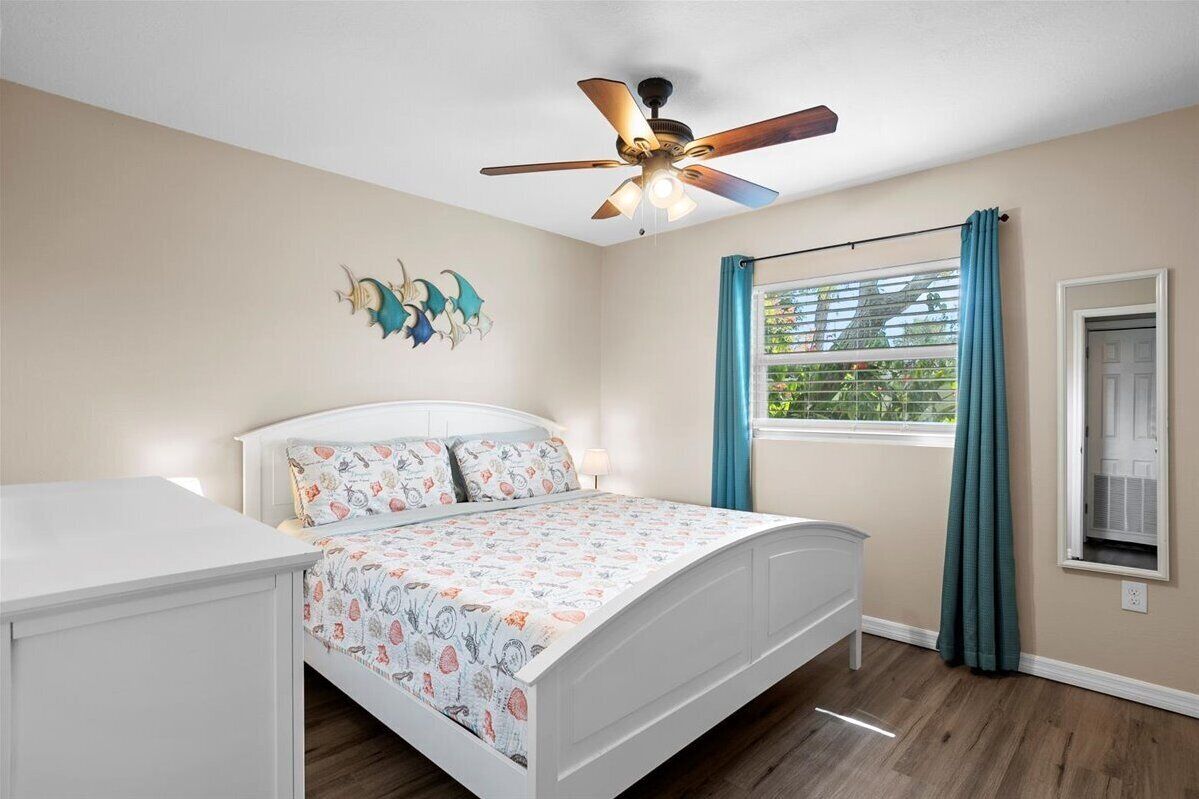 Une chambre à coucher avec un lit, un ventilateur de plafond, une fenêtre avec des rideaux et un élément décoratif mural.