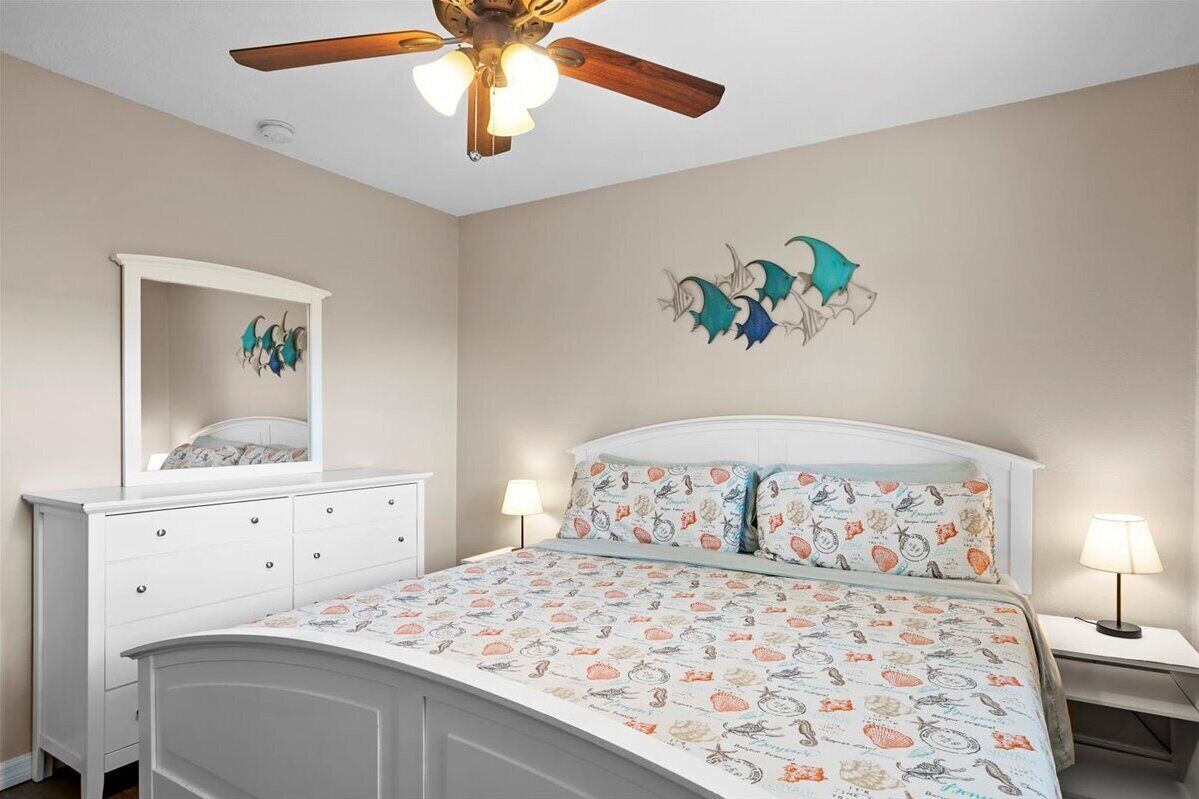 A bedroom with a bed, a dresser, a nightstand, a ceiling fan, and wall art.