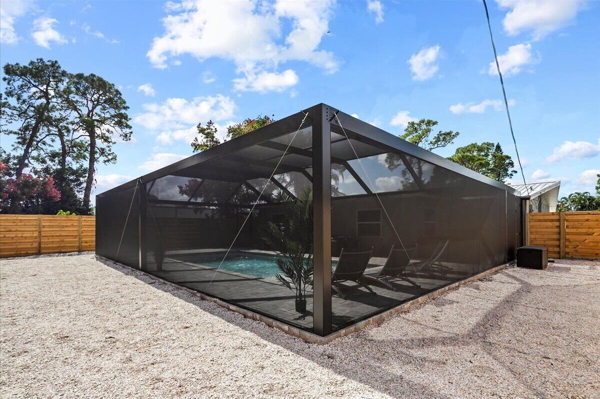 Un espace extérieur moderne et aménagé, doté d’une piscine, entouré d’une zone recouverte de gravier et délimité par une clôture en bois.