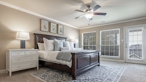 Une chambre à coucher comprenant un lit, des tables de chevet, un ventilateur de plafond et une grande fenêtre avec des stores.