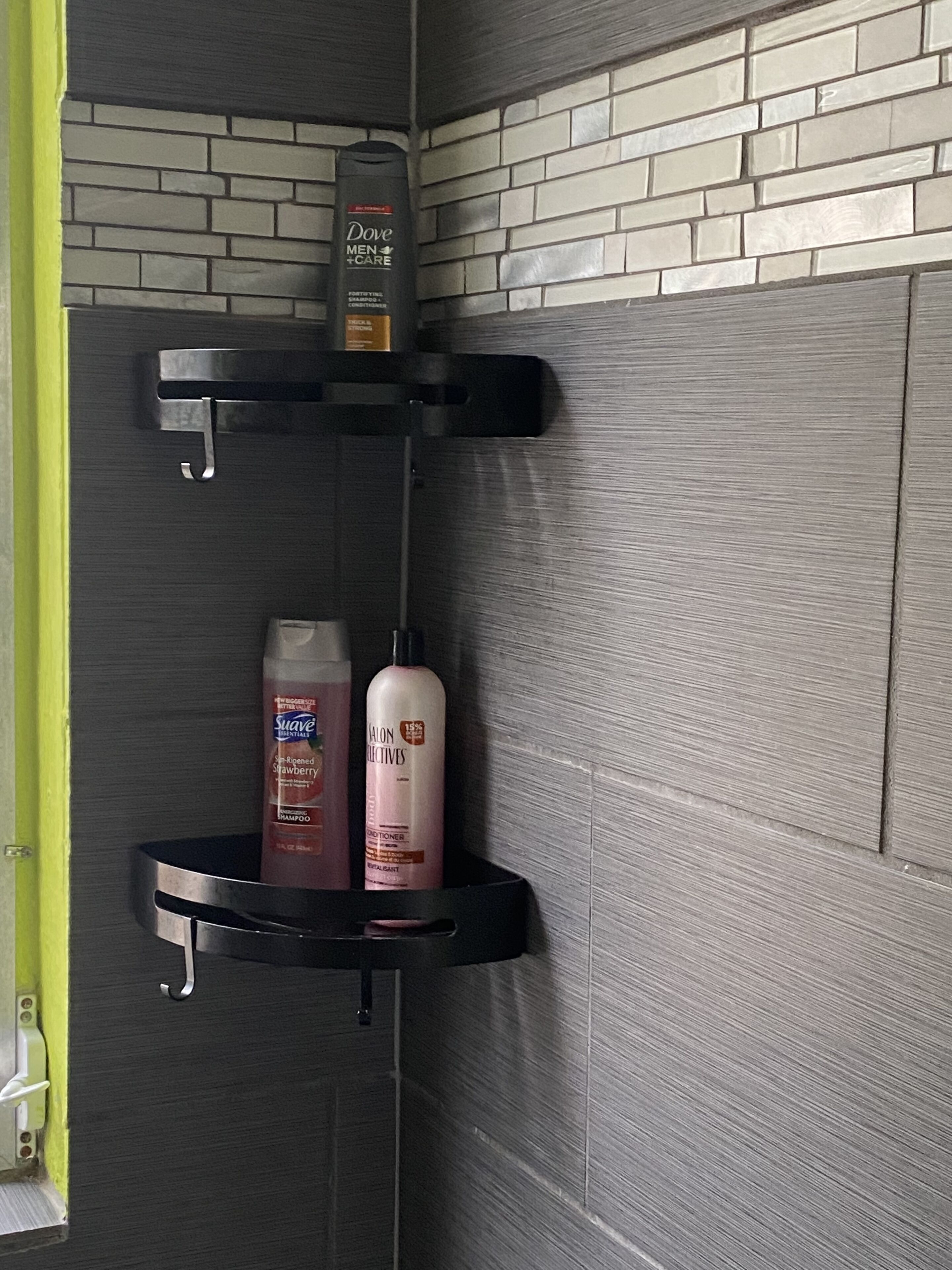 Een badkamer met een betegelde muur, een zwart schap met Dove Men+Care lotion, Suave shampoo en een fles lotion.