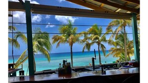 A bar area with a view of the ocean and palm trees. - Tropical one bedroom condo steps from pool. (Christiansted)