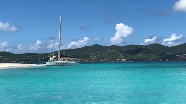 A boat named RENEGADE on clear turquoise waters with a beach and green hills in the background. - Tropical one bedroom condo steps from pool. (Christiansted)