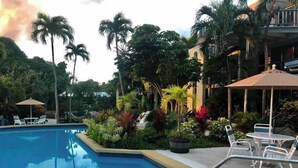 A swimming pool surrounded by lush greenery and outdoor seating areas. - Tropical one bedroom condo steps from pool. (Christiansted)
