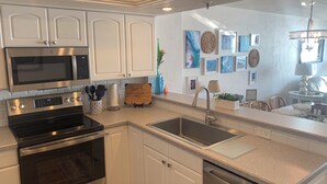 Una cocina moderna con armarios blancos, electrodomésticos de acero inoxidable y encimera de granito, junto con un comedor con candelabro.