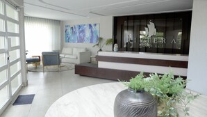 A modern hotel lobby with a reception desk, seating area, and a large abstract painting. - Amazing view at Riviera Colonial & zona Colonial (Villa Duarte)