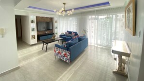 A modern living room with a blue sofa, a coffee table, and a TV mounted on the wall. - Amazing view at Riviera Colonial & zona Colonial (Villa Duarte)