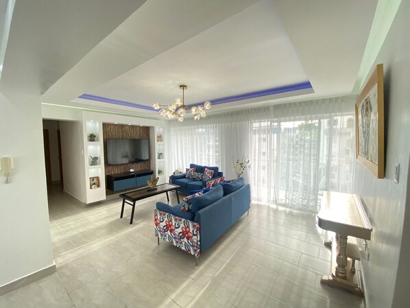 A modern living room with a blue sofa, a coffee table, and a TV mounted on the wall.