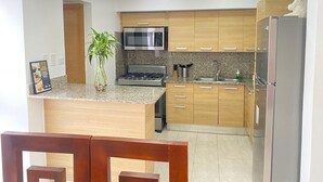 A modern kitchen with wooden cabinets, a stainless steel refrigerator, a microwave, and a gas stove. - Amazing view at Riviera Colonial & zona Colonial (Villa Duarte)