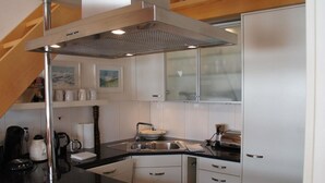 Una cocina moderna con armarios blancos, una campana de acero inoxidable, un fregadero y una cafetera.