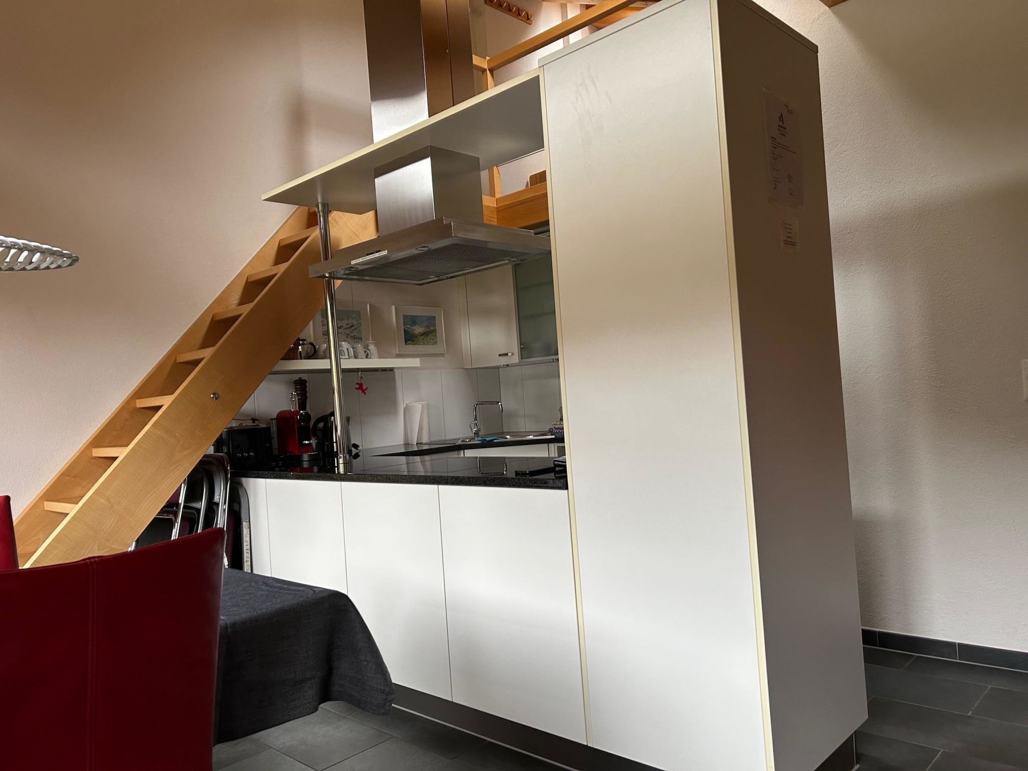 A modern kitchen with white cabinets, a wooden staircase, and a grey bench.