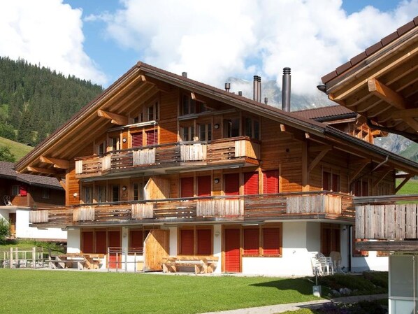 Un chalet en bois à plusieurs étages, doté de balcons, d’une terrasse couverte et surplombant un paysage montagneux.