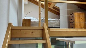 Un dormitorio estilo loft con una escalera de madera, una cama litera y una zona de cocina abajo.