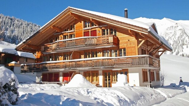 Un chalet de madera de varios pisos con balcones, ubicado en una zona montañosa nevada.
