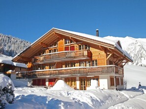 Un chalet en bois à plusieurs étages, doté de balcons, situé dans une région montagneuse enneigée.