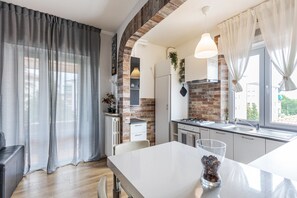 A modern kitchen with a brick wall, white cabinets, a large window, and a dining area with a table and chairs.