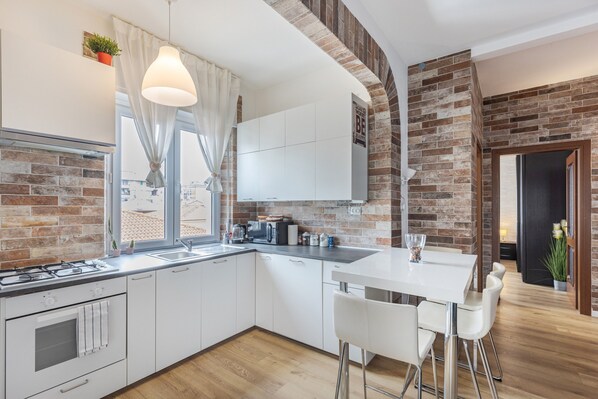 Une cuisine moderne avec des meubles blancs, un mur d’accent en briques et un coin repas comprenant une table blanche et des tabourets de bar.