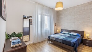 Een slaapkamer met een bed, nachtkastjes, een spiegel en een raam met gordijnen.