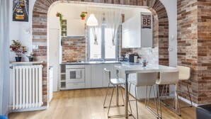 Een moderne keuken met een bakstenen boog, witte kasten en een bar met krukken.