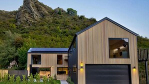 Et moderne hus i to etager med garage, store vinduer og udsigt til et bjergrigt landskab.