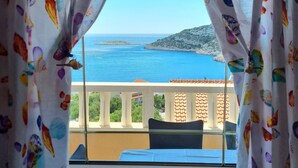 En balkon med udsigt over havet og et bjergrigt landskab.