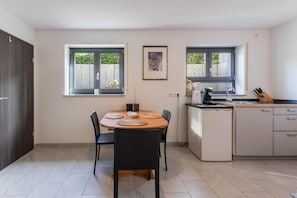 Une cuisine moderne avec une table à manger, des chaises, un réfrigérateur et une fenêtre donnant sur un espace verdoyant.