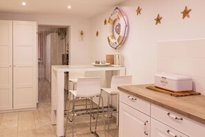 A modern kitchen with white cabinetry, a wooden countertop, and a bar area with white chairs.