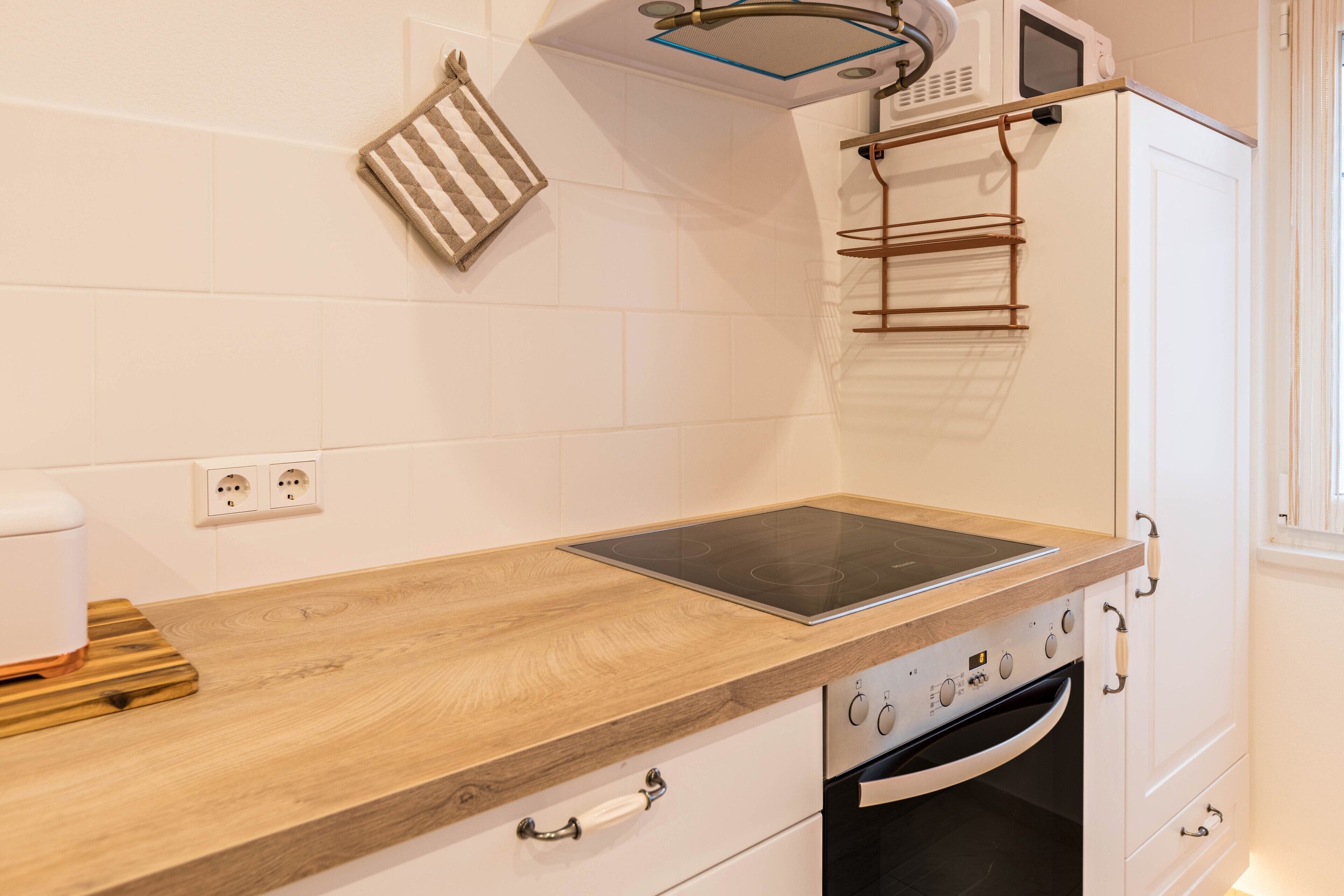 Eine Küche mit Holzarbeitsplatte, Backofen, Mikrowelle und einer hängenden Stange.