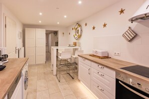 A modern kitchen with white cabinets, a wooden countertop, a built-in oven, and a wall-mounted stove.