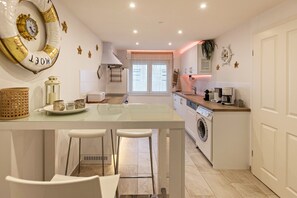 A modern kitchen with a central island, bar stools, a washing machine, and a coffee machine.