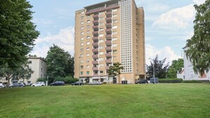 A multi-story residential building with a flat roof, surrounded by a grassy area and parked cars.