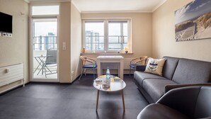 A living room with a sofa, a coffee table with a bottle and glasses, a dining table with chairs, and a large window with a city view.