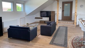 Un salon moderne avec un téléviseur, des canapés, une table basse en verre, un plancher en bois et un escalier menant à une autre pièce.