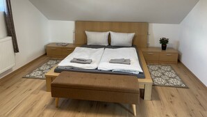 Une chambre à coucher avec un lit en bois, deux tables de chevet, une commode, un banc et une plante en pot.