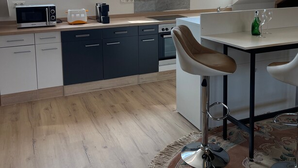 Une cuisine moderne équipée d’un four à micro-ondes, d’un grille-pain et d’un four, dotée de grandes fenêtres et comprenant un coin repas avec une chaise.