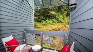 Een balkon met twee witte stoelen, waarvan er één een rode kussen heeft, en een klein tafeltje met een wit bord.