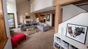 Een ruime woonkamer met een grijze modulaire bank, rode poefs en een boekenkast vol boeken.