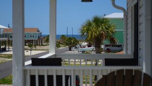 Une véranda dotée d’un ventilateur de plafond, donnant sur une plage où l’on aperçoit un bateau et des palmiers.