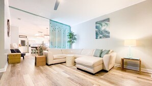 Un salon moderne avec un canapé d’angle, une petite table ronde et une lampe posée sur une table d’appoint.
