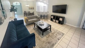 Een woonkamer met een bank, salontafel, televisie en een eethoek op de achtergrond.