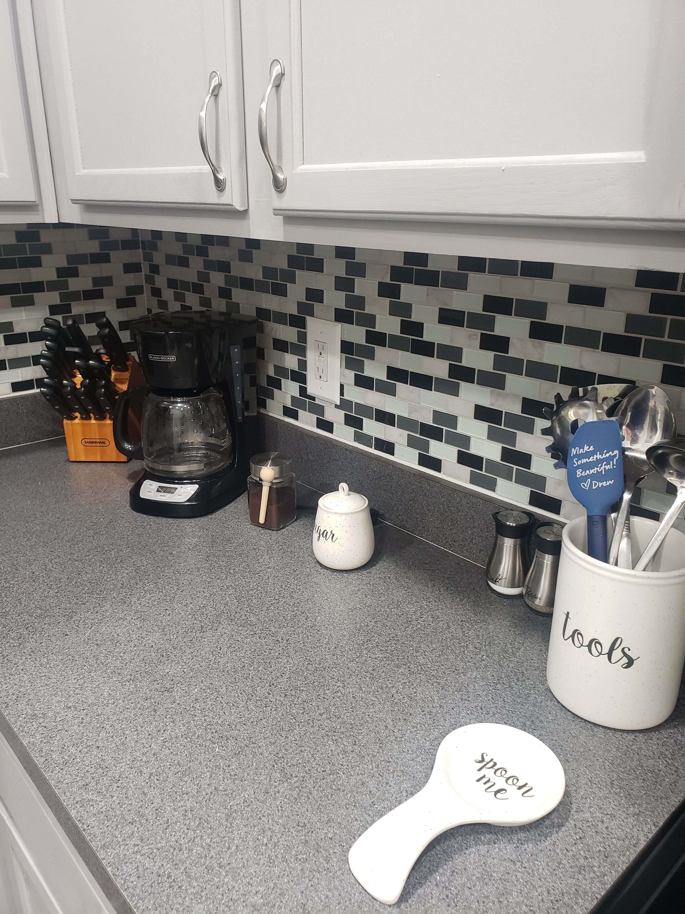 A kitchen counter with a coffee maker, sugar container, spice jars, and a utensil holder.