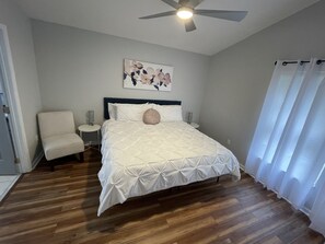 Ein Schlafzimmer mit einem Bett, einem Sessel, einem Deckenventilator und einem Gemälde an der Wand.