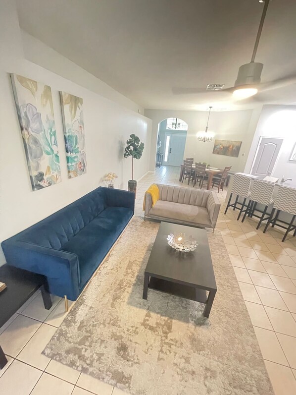 Ein Wohnzimmer mit einem blauen Sofa, einem beigen Sofa, einem Couchtisch und einem Essbereich mit Tisch und Stühlen.