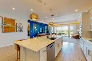 A modern kitchen with a central island, white cabinetry, and a large window providing a view of the outdoors.
