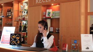 Een receptie met een houten receptiebalie, een digitale klok en een bord boven de balie met de tekst 