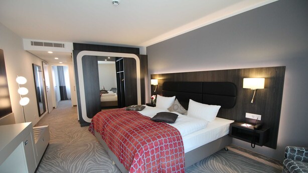 Een moderne hotelkamer met een groot bed, een nachtkastje, een spiegel en een rood bed met een patroon.