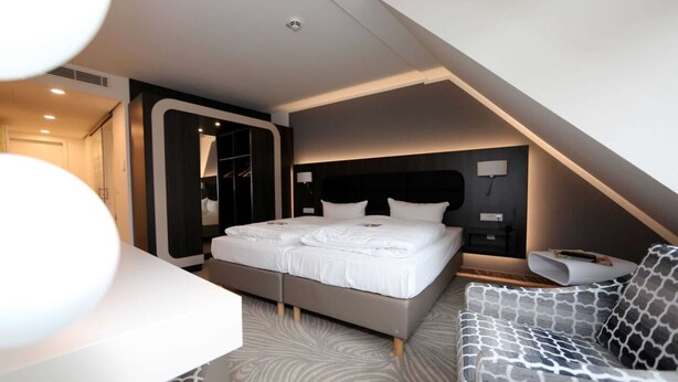 A modern bedroom with a large bed, a sofa, and a walk-in closet.